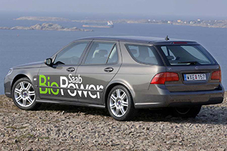 Gray hatchback car with Saab BioPower logo parked on a rocky overlook overlooking the water.