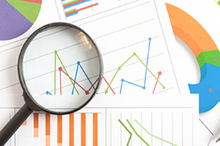 Pile of papers with line charts, bar charts, and pie charts with a magnifying glass on top.