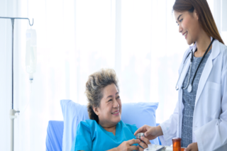 Young smiling nurse giving medication to happy older female patient.