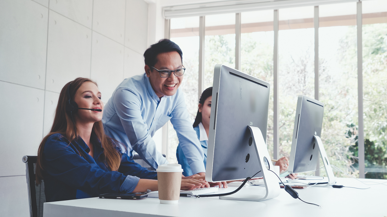 Instructor training two individuals on process improvement techniques on a computer.