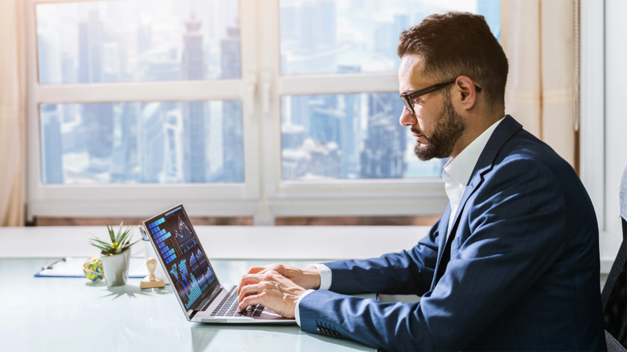 Business man in a suit at a desk using a business intelligence platform to analyze data on his  laptop.