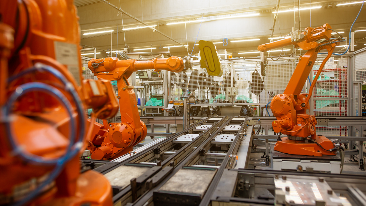 Orange industrial automatic robot arms in the production line of a factory.