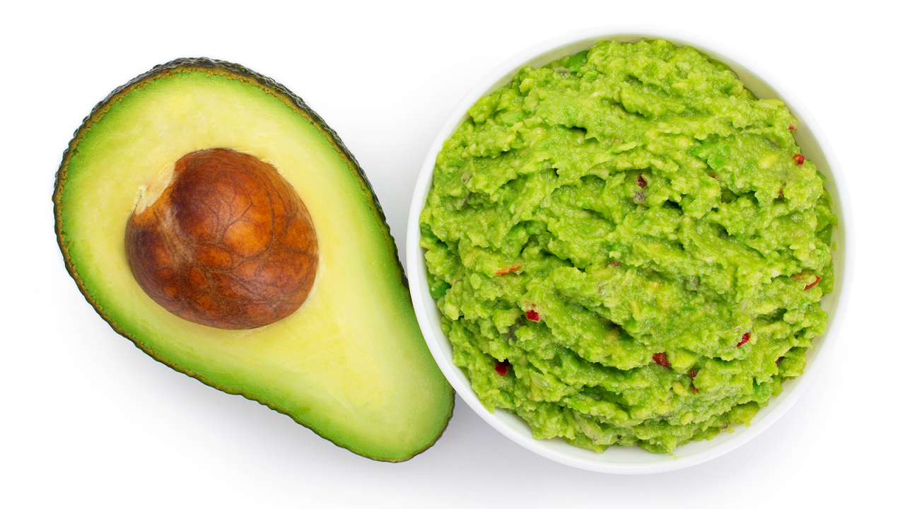 Tigela de guacamole fresco ao lado da metade de um abacate com o caroço.